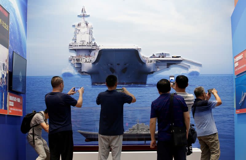 FILE PHOTO: Visitors hold their mobile phones in front of exhibits showing aircraft carrier Liaoning, during an exhibition on China's achievements marking the 70th anniversary of its founding at the Beijing Exhibition Center, in Beijing