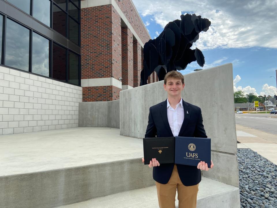 Luke Monk stands in front of the Northside High School bear mascot with his associates degree from UAFS and acceptance letter from Westpoint U.S. Military Academy.