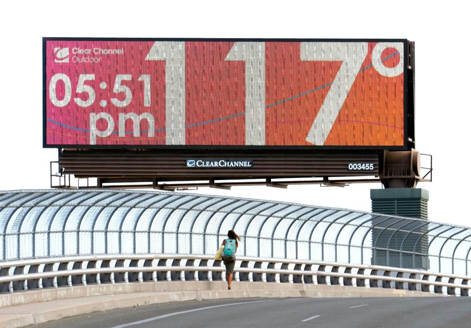 A pedestrian walks down Seventh Street in Phoenix on July 18, 2023, as the temperature of 117 degrees is displayed on a digital billboard.