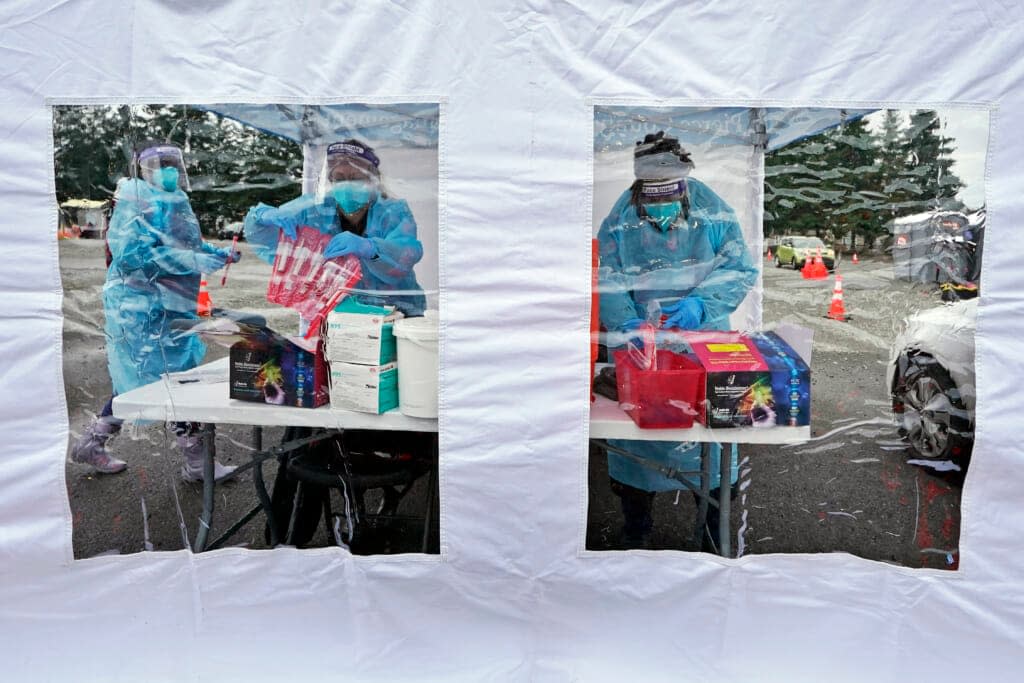Workers at a drive-up COVID-19 testing clinic stand in a tent as they prepare PCR coronavirus tests, Jan. 4, 2022, in Puyallup, Wash., south of Seattle. (AP Photo/Ted S. Warren, File)