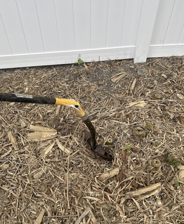 Shovel digging into soil and mulch near a white fence
