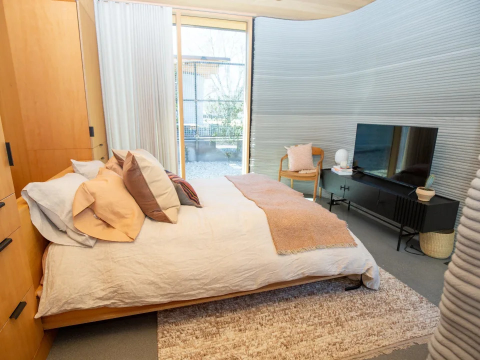 The bedroom inside the House Zero accessory dwelling unit. There's a bed, TV, and large windows.