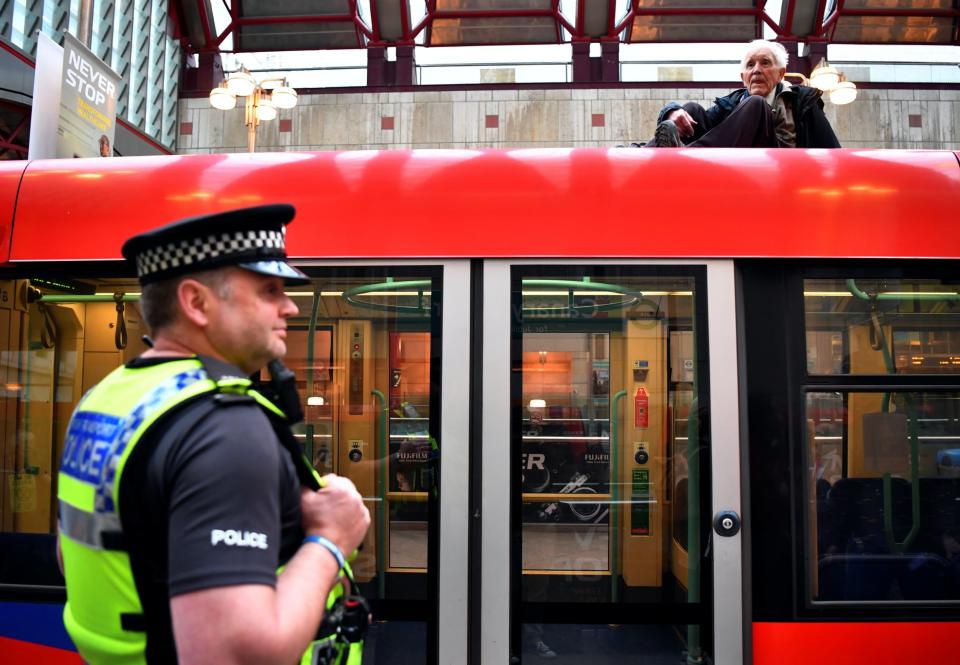 Phil Kingston, 83, sits on top of a DLR train as a police officer watches on (Dylan Martinez/Reuters)