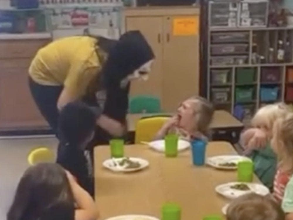 woman scaring little girl while wearing a halloween mask