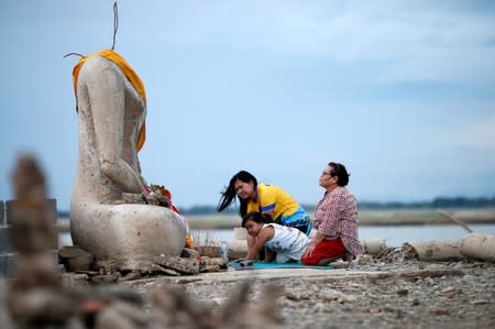 A family prays near the ruins of a headless Buddha statue, which has resurfaced in a dried-up dam due to drought, in Lopburi, Thailand