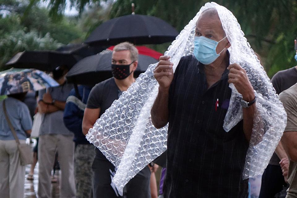 Voters, including Julio Resto, right, of Boca Raton, wait in the rain to vote at the Spanish River Library in Boca Raton, Monday, Oct. 19, 2020, on the first day of early voting in Florida. (Zach Sobiech/South Florida Sun-Sentinel via AP) ORG XMIT: FLLAU602