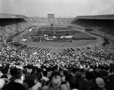 FILE - This July 29, 1948 file photo, showing the opening ceremony of the 1948 Olympic Games at Wembley Stadium, in London, England. London was still cleaning up bombing damage from World War II when it staged the Olympics in 1948. Britain was also struggling financially; food, clothing and gas were still being rationed. The athletes had to bring their own towels and, with housing in short supply, were accommodated in schools and Royal Air Force camps. The games were organized in less than two years, and despite the tiny budget it was a success, its legacies including greater sporting opportunities for women. (AP Photo, File )