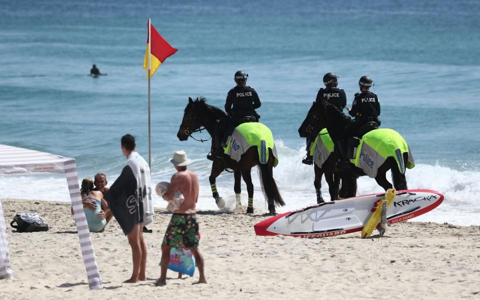 Police officers ride horses on Coolangatta beach, along the New South Wales and Queensland border during an anti-lockdown protes - Shutterstock