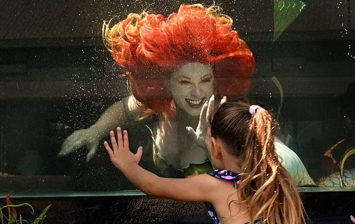 In her new, portable mermaid tank, Aurora Rose Watkins as Mermaid Nellie, captivates the attention of Georgia Gordon, 6, during a promotional video shoot.