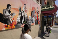 Two women walk along Jackson Street in Chinatown past the new "AAPI Community Heroes" mural in San Francisco, Monday, May 23, 2022. Chinatowns and other Asian American enclaves across the U.S. are using art and culture to show they are safe and vibrant hubs nearly three years after the start of the pandemic. From an inaugural arts festival in San Francisco to night markets in New York City, the rise in anti-Asian hate crimes has re-energized these communities and drawn allies and younger generations of Asian and Pacific Islander Americans. (AP Photo/Eric Risberg)