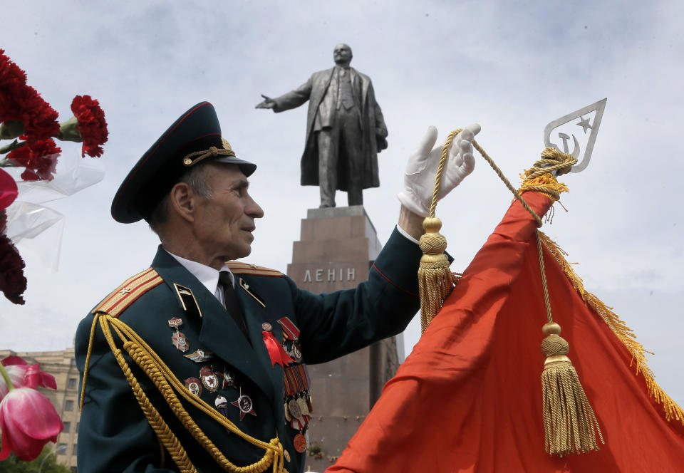 A former Soviet Union army veteran prepares a Soviet army flag as a symbol of victory, in front of the monument of Soviet revolutionary leader Vladimir Lenin, during a Victory Day celebration, which commemorates the 1945 defeat of Nazi Germany, in Kharkiv, Ukraine, Friday, May 9, 2014. Putin's surprise call on Wednesday for delaying the referendum in eastern Ukraine appeared to reflect Russia's desire to distance itself from the separatists as it bargains with the West over a settlement to the Ukrainian crisis. But insurgents in the Russian-speaking east defied Putin's call and said they would go ahead with the referendum. (AP Photo/Efrem Lukatsky)