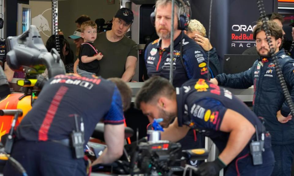 Elon Musk holding one of his children while members of a Red Bull crew work on a car at the Miami Grand Prix in May 2023