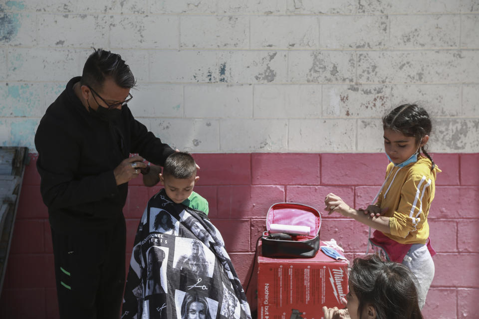 A barber cuts a child's hair at the Kiki Romero Sports Complex migrant shelter in Ciudad Juarez, Mexico, Wednesday, April 21, 2021. Mexico said it is planning to set up 17 shelters for underage migrants along the country's southern border, as well as some along the northern border with the United States, amid a wave of child migrants coming from Central America. (AP Photo/Christian Chavez)