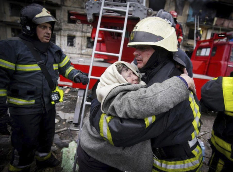 In this photo released by Ukrainian State Emergency Service, a firefighter hugs an elderly woman after evacuation from an apartment building hit by shelling in Kyiv, Ukraine, Monday, March 14, 2022. (Ukrainian State Emergency Service via AP)