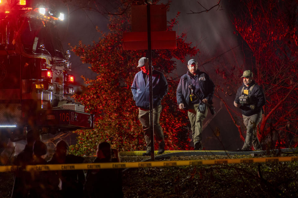 Fire and police officials walk around the scene of a house explosion as an Arlington County Fire Department ladder truck sprays water down on the remains of the building on Monday, Dec. 4, 2023, in Arlington, Va. (AP Photo/Kevin Wolf)