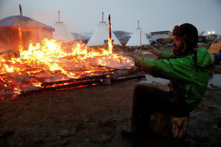 An opponent of the Dakota Access oil pipeline warms his hands beside a building set on fire by protesters preparing to evacuate the main opposition camp against the pipeline near Cannon Ball, North Dakota, U.S., February 22, 2017. REUTERS/Terray Sylvester