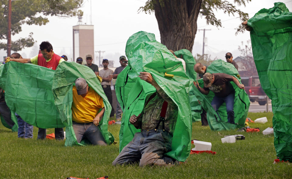 FILE - In this Aug. 22, 2015 file photo, volunteers learn to deploy fire shelters with practice equipment after a callout by fire officials seeking to supplement their usual resources in Omak, Wash. After flames trapped 14 firefighters in California and they had to use last-resort fire shelters to survive, questions are emerging about how well the emergency devices work and how often they are used while crews fight wildfires. (AP Photo/Elaine Thompson, File)