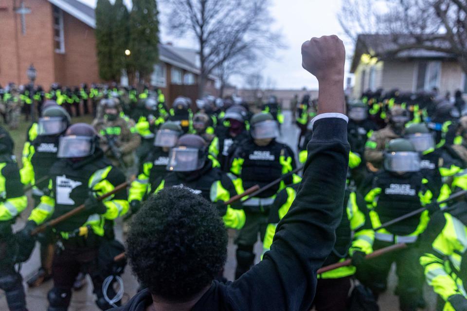 <p>A man raises his fist as he faces the Minnesota State Troopers standing guard outside the Brooklyn Center Police Station after a police officer shot and killed 20-year-old Daunte Wright during a traffic stop in Brooklyn Center, Minneapolis, Minnesota on April 12, 2021</p> (Photo by KEREM YUCEL/AFP via Getty Images)