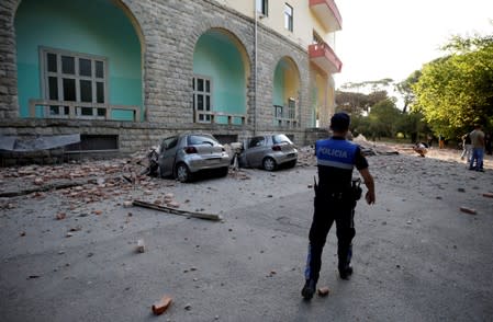 A police officer walks past destroyed cars and a damaged building after an earthquake in Tirana