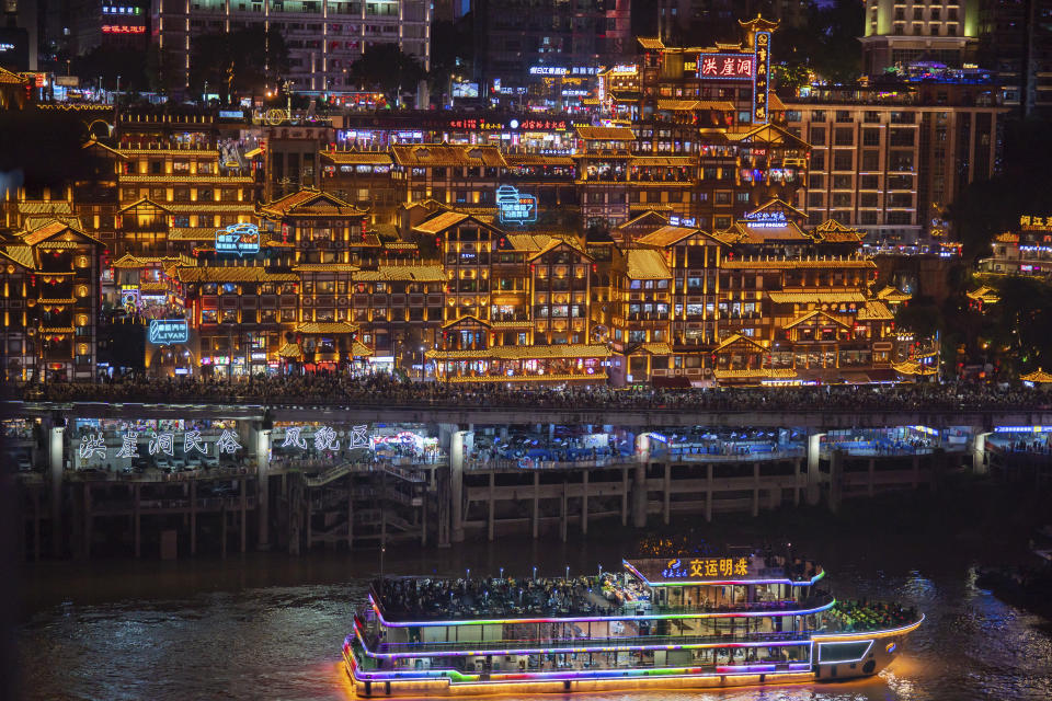 A ferry carries passengers by illuminated Hongyadong cluster of traditional looking buildings crowded with tourists during a weeklong national holiday in southwest China's Chongqing Municipality on Sept. 30, 2023. Tourism in China bounced back to pre-pandemic levels during a recent eight-day national holiday, giving a temporary boost to the nation's flagging economy. (Chinatopix via AP)