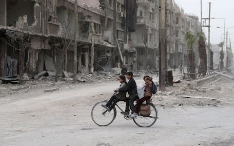 Syrian children ride a bike in a destroyed street as civilians and rebels prepare to evacuate one of the few remaining rebel-held pockets in Arbin, in Eastern Ghouta  - Credit: AFP