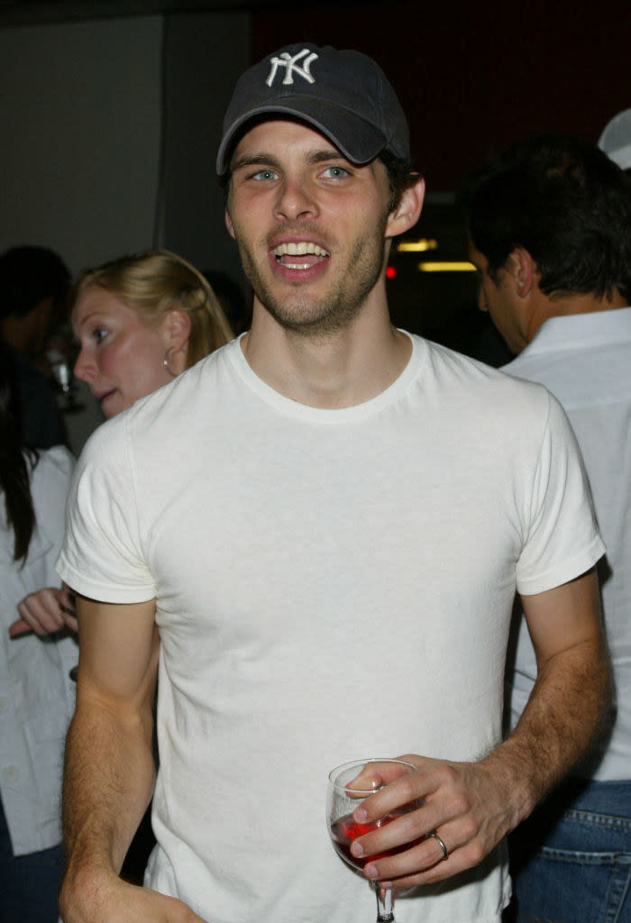 Wearing a cap and short-sleeved T-shirt and holding a glass of wine