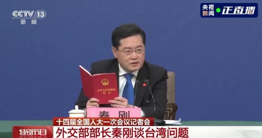 秦剛今在記者會上，拿出中國《憲法》翻閱，並引述起內容，「台灣是中華人民共和國的神聖領土的一部分。」（翻攝自央視）