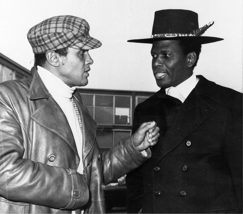 This black and white photo shows two men sporting colorful outfits having a conversation.