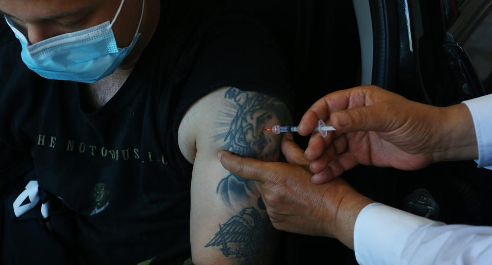 A photo of a man giving a man a Covid vaccination in his car. 