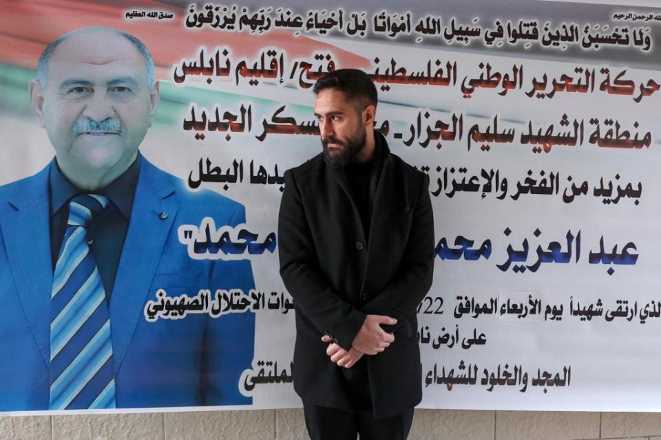 Palestinian nurse Elias al-Ashqar stands by a billboard bearing an obituary for his father Abdel Aziz, on February 24, 2023, who died during an Israeli raid in Nablus in the occupied West Bank two days earlier. - When Israel conducted its deadliest raid in the occupied West Bank in almost twenty years on February 22, a young Palestinian nurse rushed to help. Yet as critical cases succumbed to their wounds, Al-Ashqar, 25, realised one of those among the eleven killed and more than 80 injured by gunshot wounds in the daylight raid was his kin. (Photo by Zain Jaafar / AFP) (Photo by ZAIN JAAFAR/AFP via Getty Images)