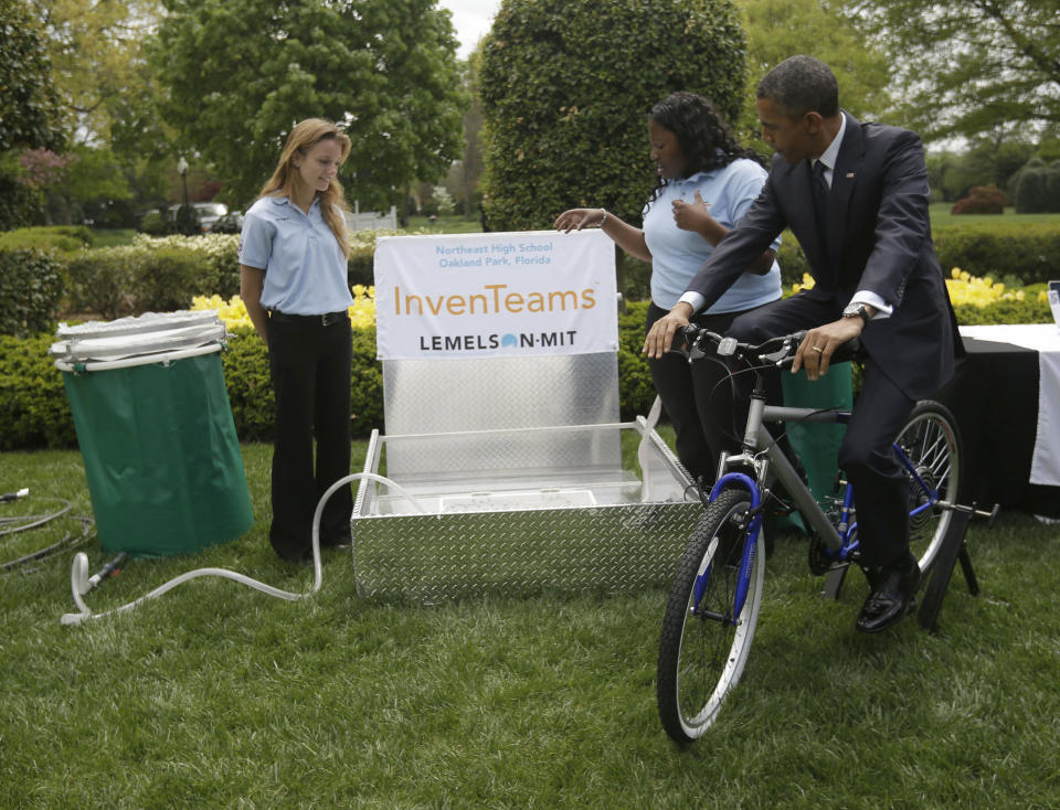 President Barack Obama pedals bicycle-powered emergency water-sanitation station for Payton Karr, 16, left, and Kiona Elliott, 18, center, both from Oakland Park, Fla., to help demonstrate their invention, Monday, April 22, 2103, in the East Garden of the White House in Washington, where the president hosted the White House Science Fair to celebrate the student winners of a broad range of science, technology, engineering and math (STEM) competitions from across the country. The bicycle filters E. Coli and other harmful pathogens from contaminated water. (AP Photo/Pablo Martinez Monsivais)