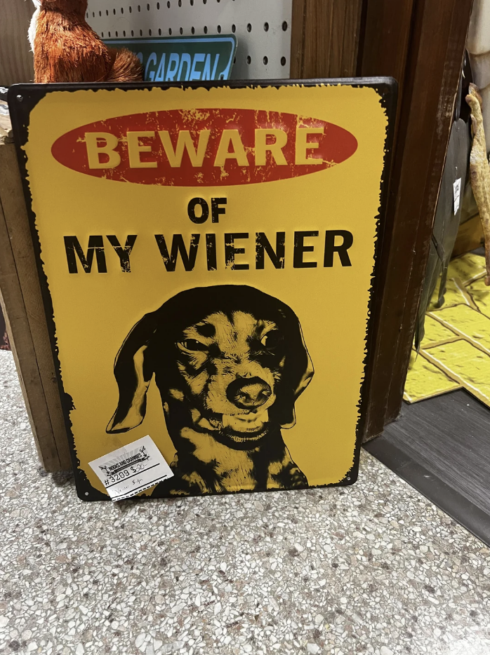 Humorous sign with "BEWARE OF MY WIENER" text and a dachshund illustration, meant as a joke for dog owners