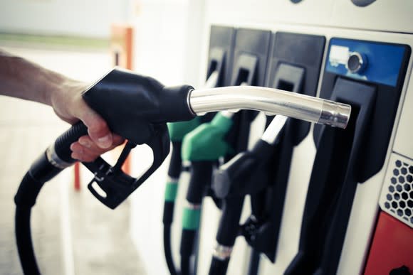 A man's hand holds a nozzle at a gas pump.