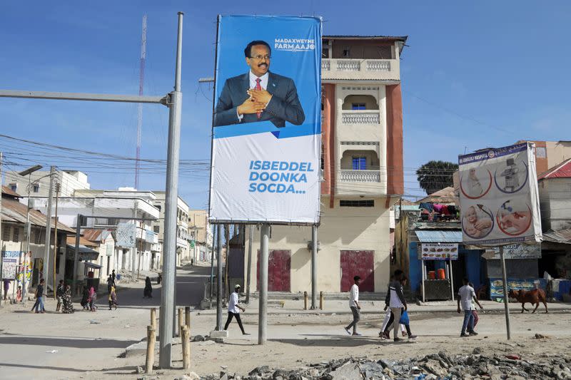 People walk past an election banner of Somali President Mohamed Abdullahi Mohamed in Mogadishu