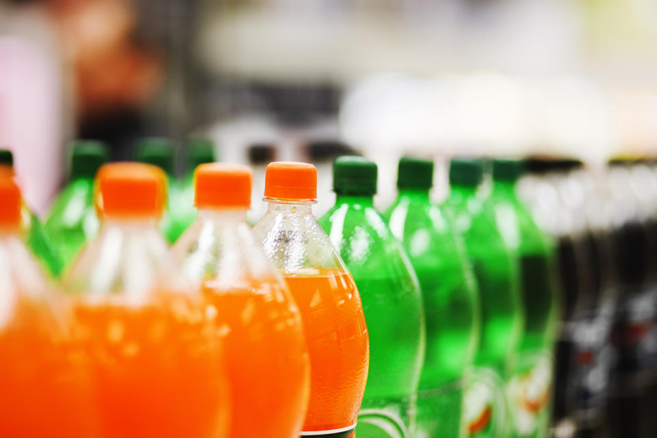 Close-up of various flavored soda bottles in a row with focus on orange soda in the foreground