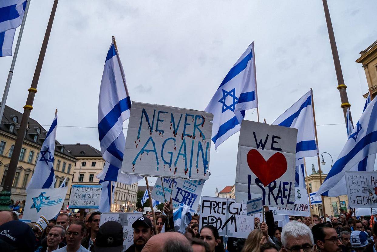 Demonstrators holding Israeli flags and signs that read both "Never Again" and "We <3 Israel." 