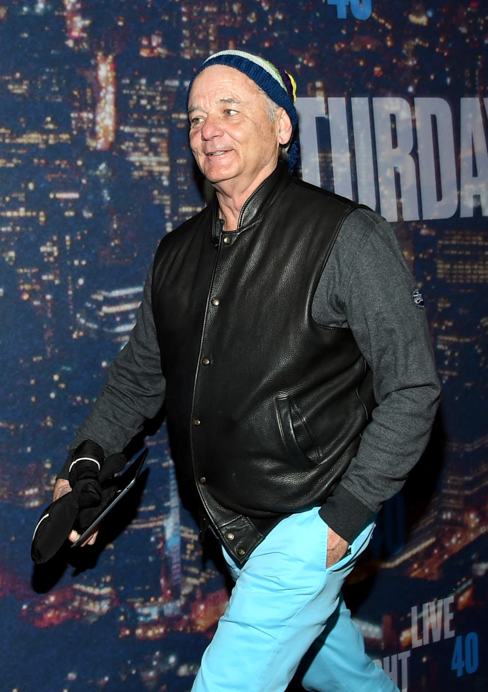 Actor Bill Murray hurries into Saturday Night Live wearing aqua tailored pants, leather varsity jacket, and a striped beanie.