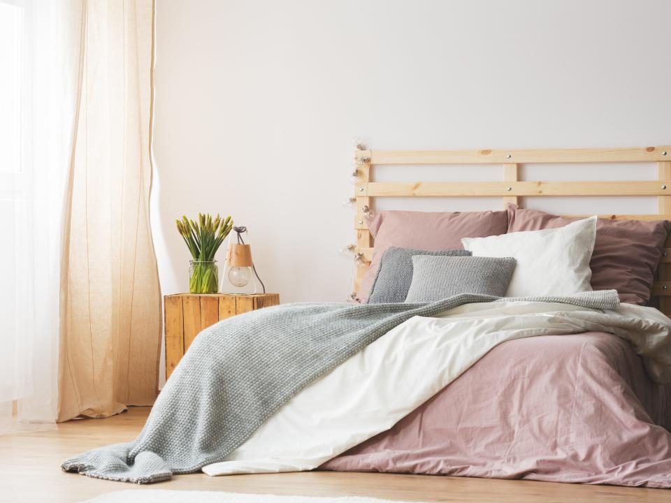 bed with white and pink sheets, with a gray throw blanket