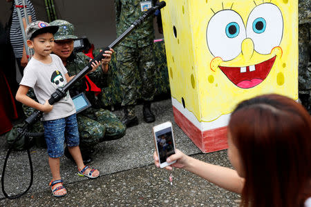 A child poses with a soldier during a public fair which displays military equipments, in Taipei, Taiwan September 29, 2018. Picture taken September 29, 2018. REUTERS/Tyrone Siu