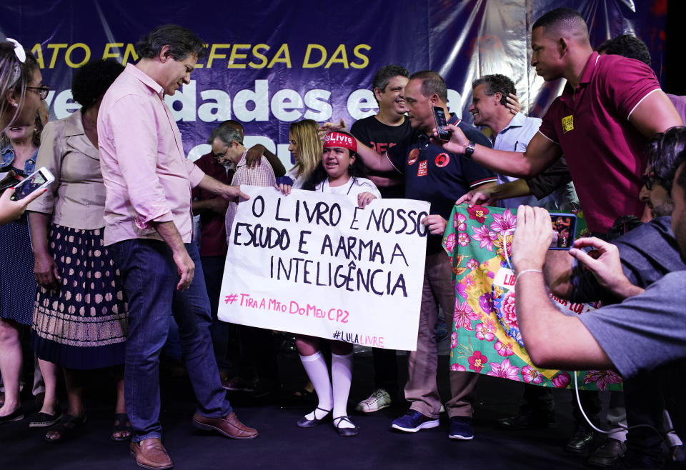 Fernando Haddad, who ran in the last presidential race backed by the Workers' Party, left, reads a sign held by a girl that reads "The book is our shield and gun of our intelligence," during a protest against cuts in Brazil's public education sector at Cinelandia square, Rio de Janeiro, Brazil, Friday, May 10, 2019. (AP Photo/Ricardo Borges)