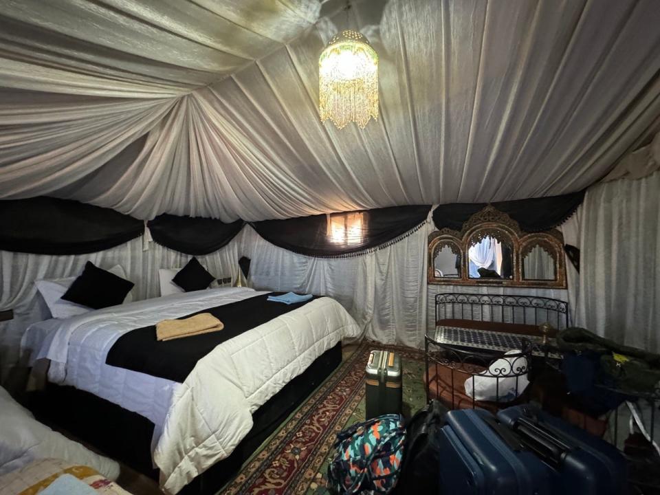 Interior of glamping tent in Sahara desert with large bed, sheet-covered ceilings, rug-covered floor