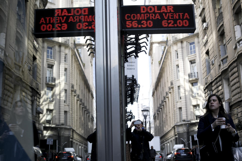 A woman walks under a sign showing exchange rates between the US dollar and Argentine peso in Buenos Aires, Argentina, Monday, Sept. 2, 2019. Argentina's government decreed on Sunday that Argentines will need authorization from the central bank for the rest of the year to buy U.S. dollars in some cases and make transfers abroad as it tries to prop up its peso currency, following a peso devaluation and ahead of an Oct. 27 election. (AP Photo/Natacha Pisarenko)