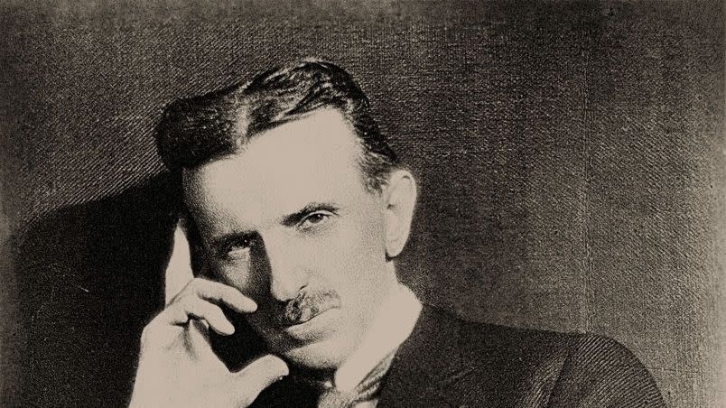 nikola tesla sitting down in a photograph and holding his head with his right hand in a thinking posture