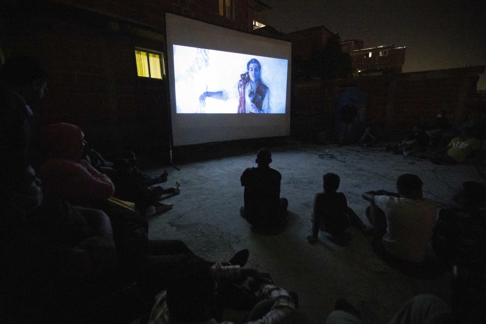 The film Aladdin is projected on a screen set up on the roof of a home in the Petare neighborhood, where residents from that home and nearby homes sit on the roof in Caracas, Venezuela, late Monday, June 1, 2020. A neighborhood group called The Download Zone set up the movie as a free entertainment option for families cooped up since mid-March under the COVID-19 quarantine. (AP Photo/Ariana Cubillos)