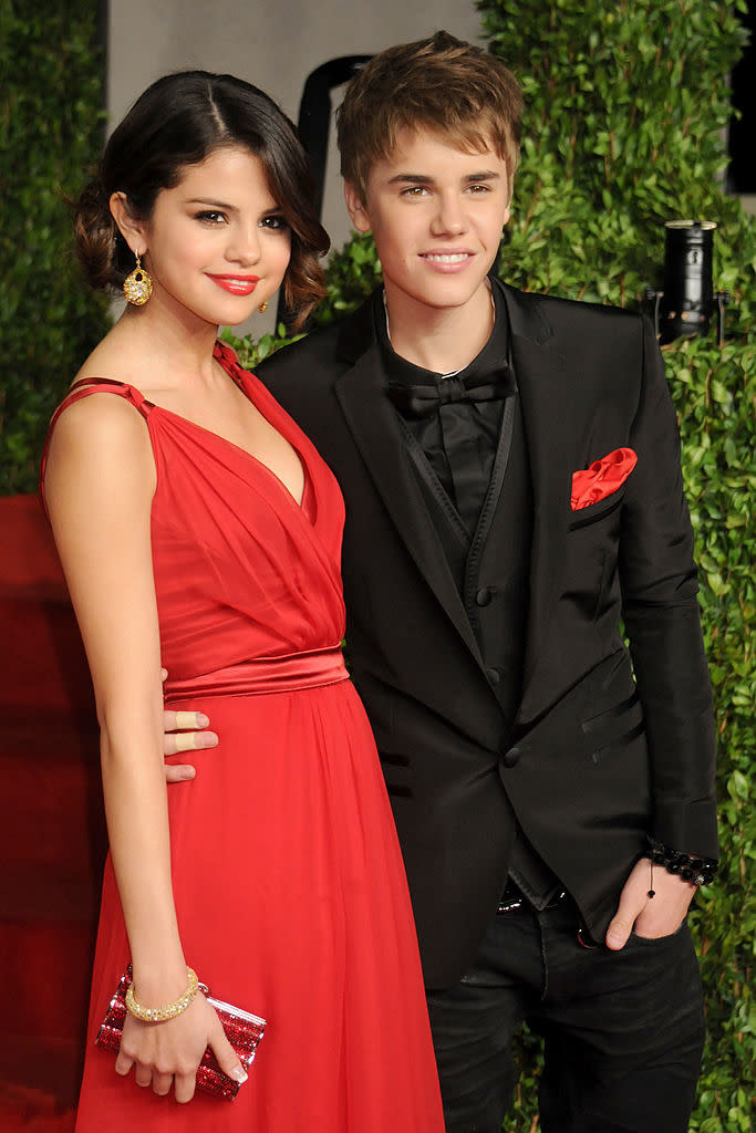 Two individuals in formal attire posing together, one in a red dress, the other in a black suit with a red pocket square