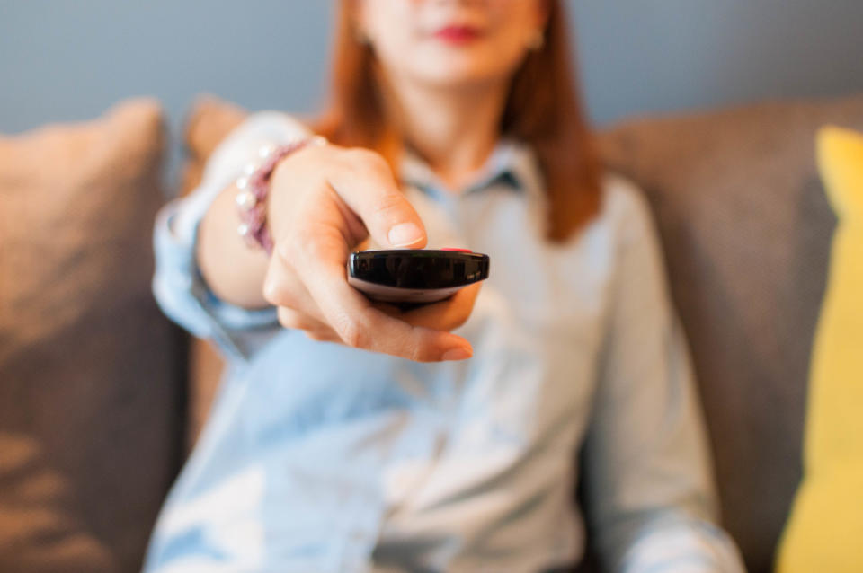 A young woman is holding a television remote control while sitting in a sofa