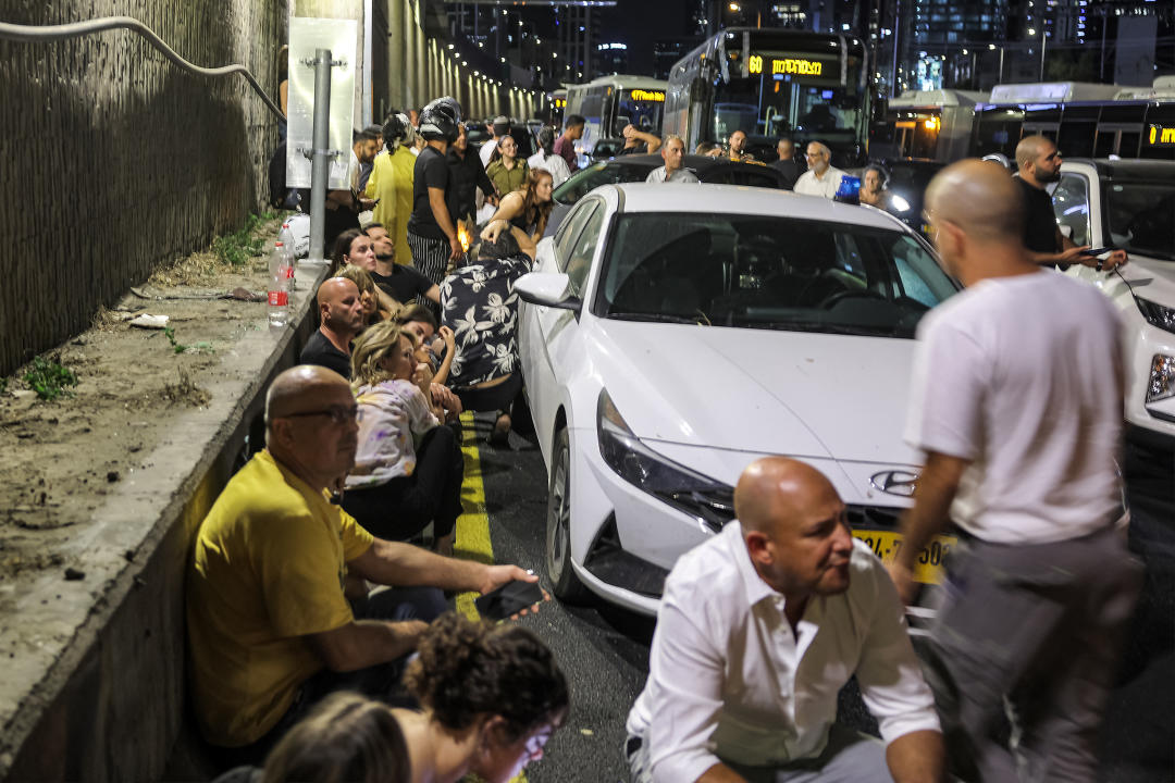 People take cover behind vehicles under a bridge along the side of a highway in Tel Aviv on October 1, 2024. Air raid sirens sounded in central Israel on October 1, the military said, a day after the army launched ground operations into southern Lebanon targeting Hezbollah positions. 