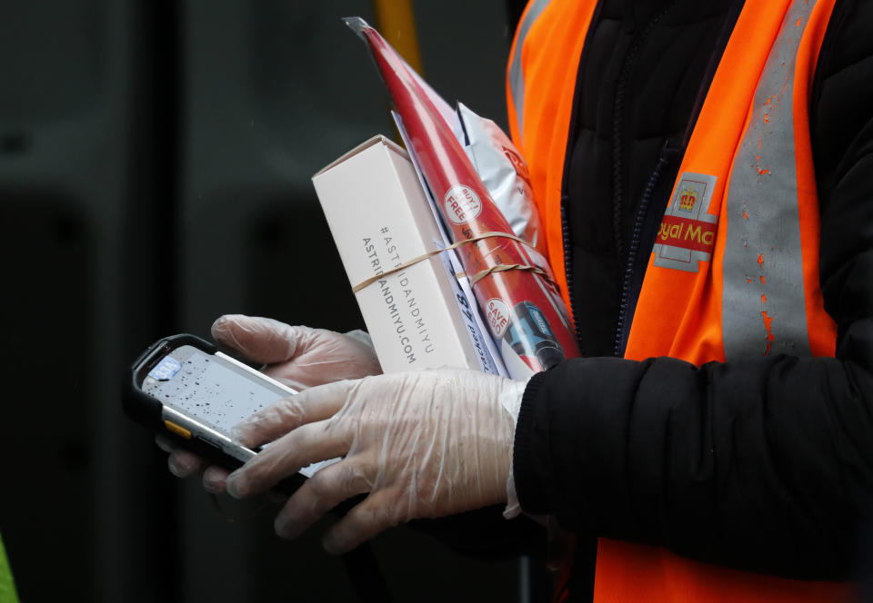 In this March 5, 2020, photo, a Royal Mail employee wears gloves as he hold parcels and the signature handheld as he delivers in London. While white collar workers trying to avoid contagion can work from home or call in sick if they experience symptoms of the new virus, such precautions are not an options for the millions of waiters, delivery workers, cashiers, ride-hailing drivers, museum attendants and countless others who routinely come into contact with the public. (AP Photo/Frank Augstein)