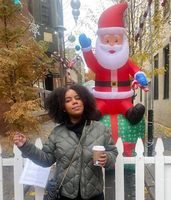 ShaLisa Pratt is shown posing with a carryout beverage in front of a large plastic Santa Claus. 