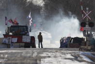 A protester stands beside smoke at the closed train tracks in Tyendinaga Mohawk Territory near Belleville, Ontario on Thursday Feb. 20, 2020, as demonstrators protest in solidarity with the Wet'suwet'en hereditary chiefs opposed to the LNG pipeline in northern British Columbia. (Lars Hagberg/The Canadian Press via AP)